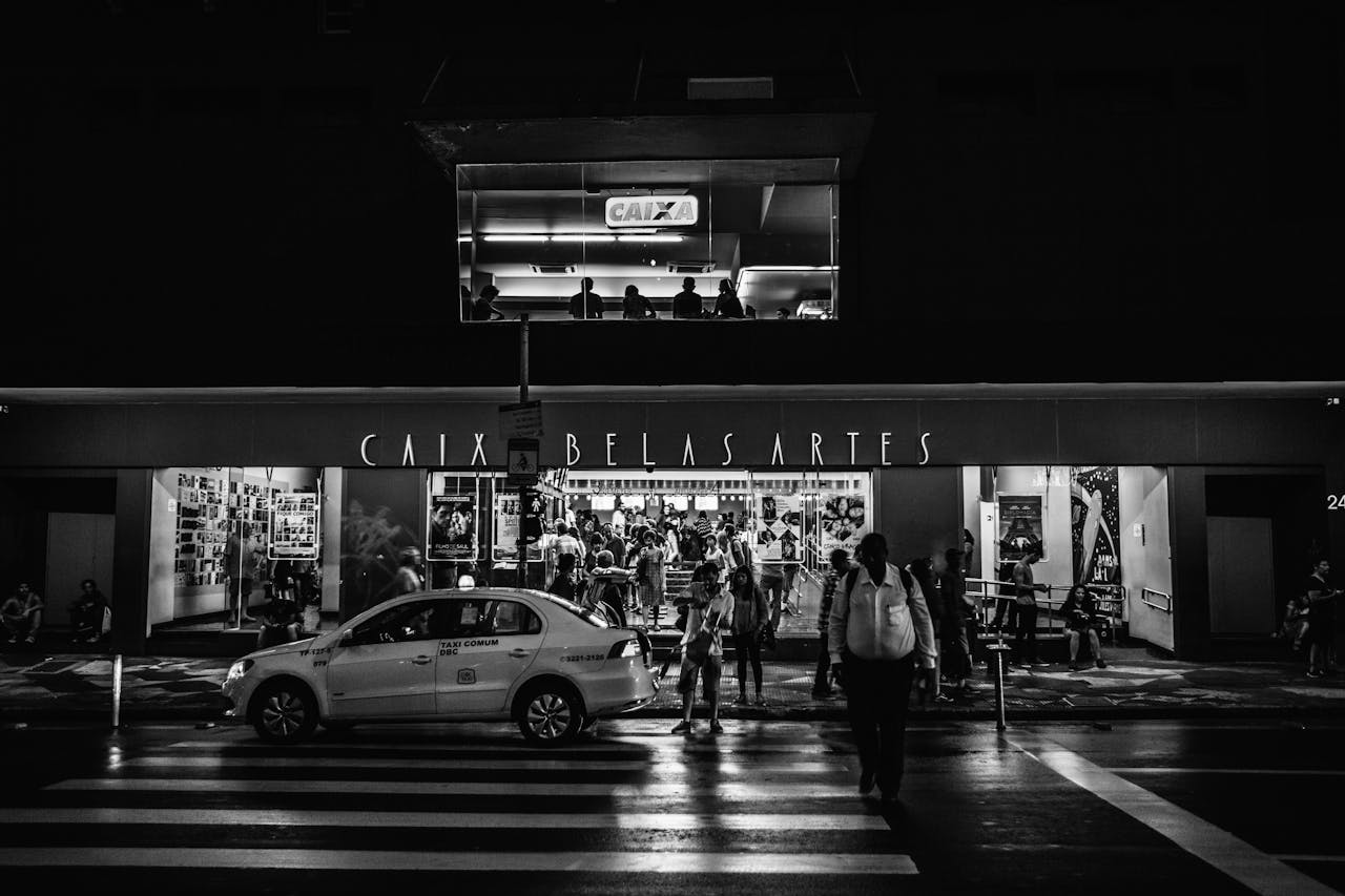 Reasons Movies Look Different Black and white image of Caixa Belas Artes cinema entrance with people and a taxi at night.